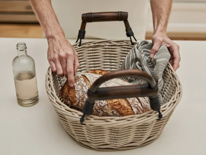 Hænder pakker en picnickurv med brød, flaske og stofserviet